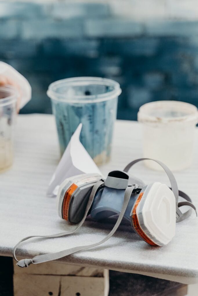 A respirator mask on a table with paint containers in an industrial workshop setting.